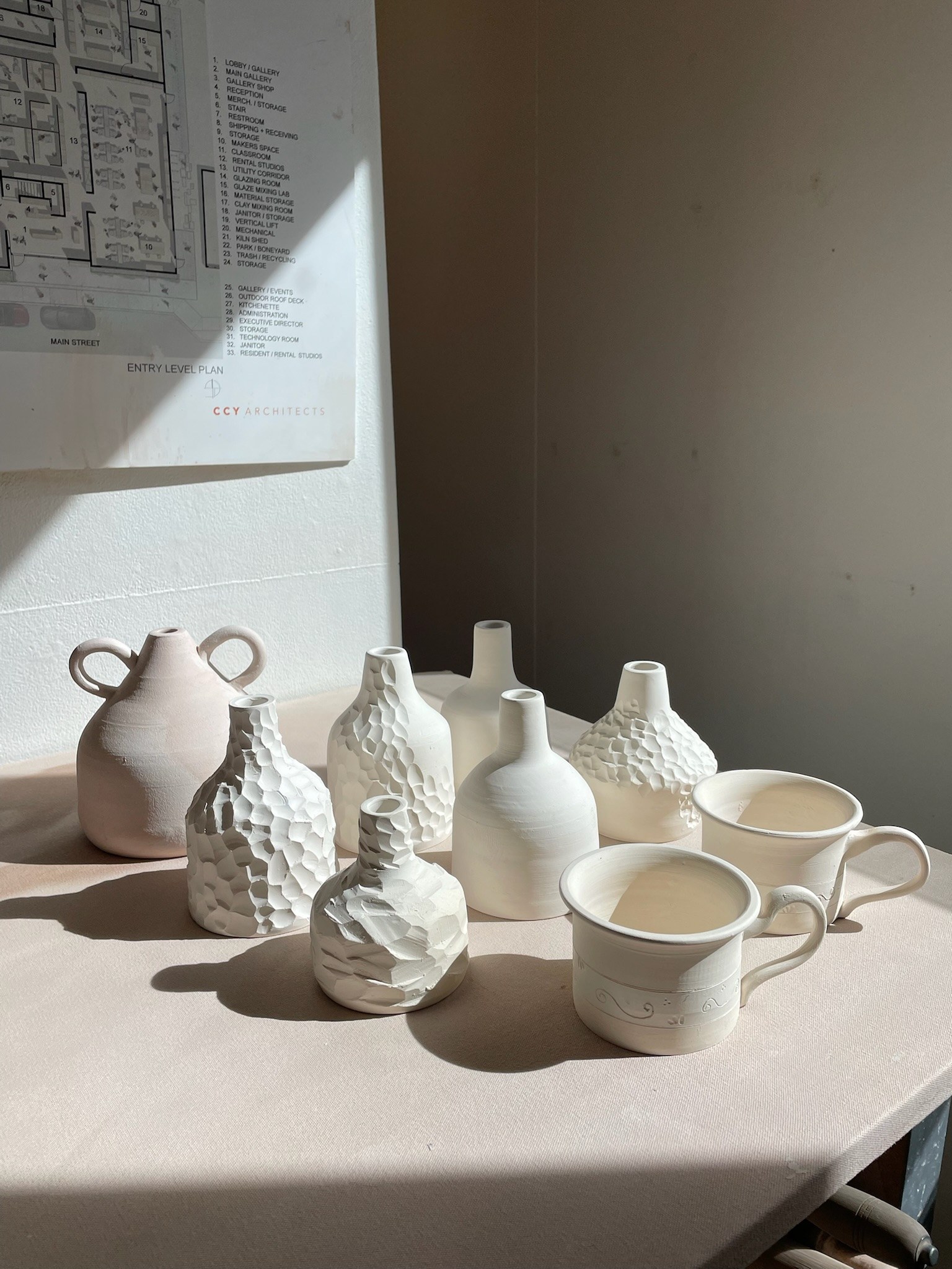 Unglazed bisque-fired pottery on a table, ready for glazing